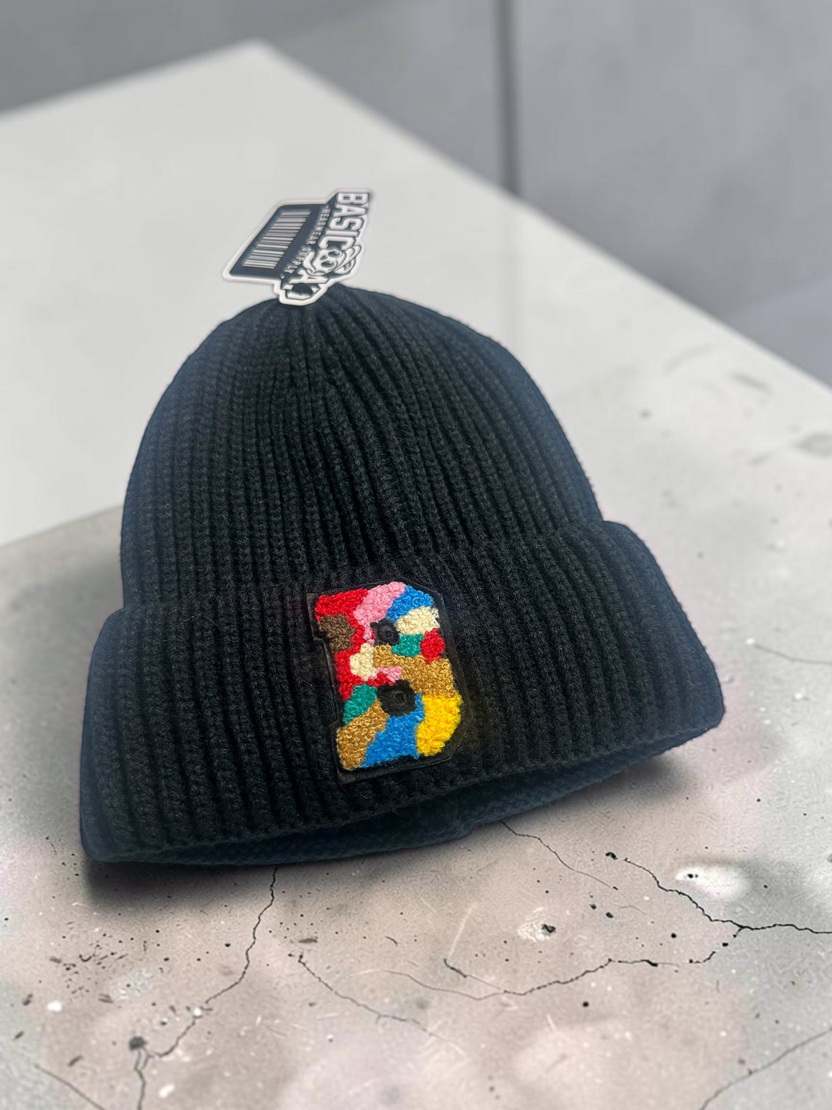 B-Is-TheBrand black ribbed knit beanie featuring a vibrant multi-colored textured B patch on the front cuff