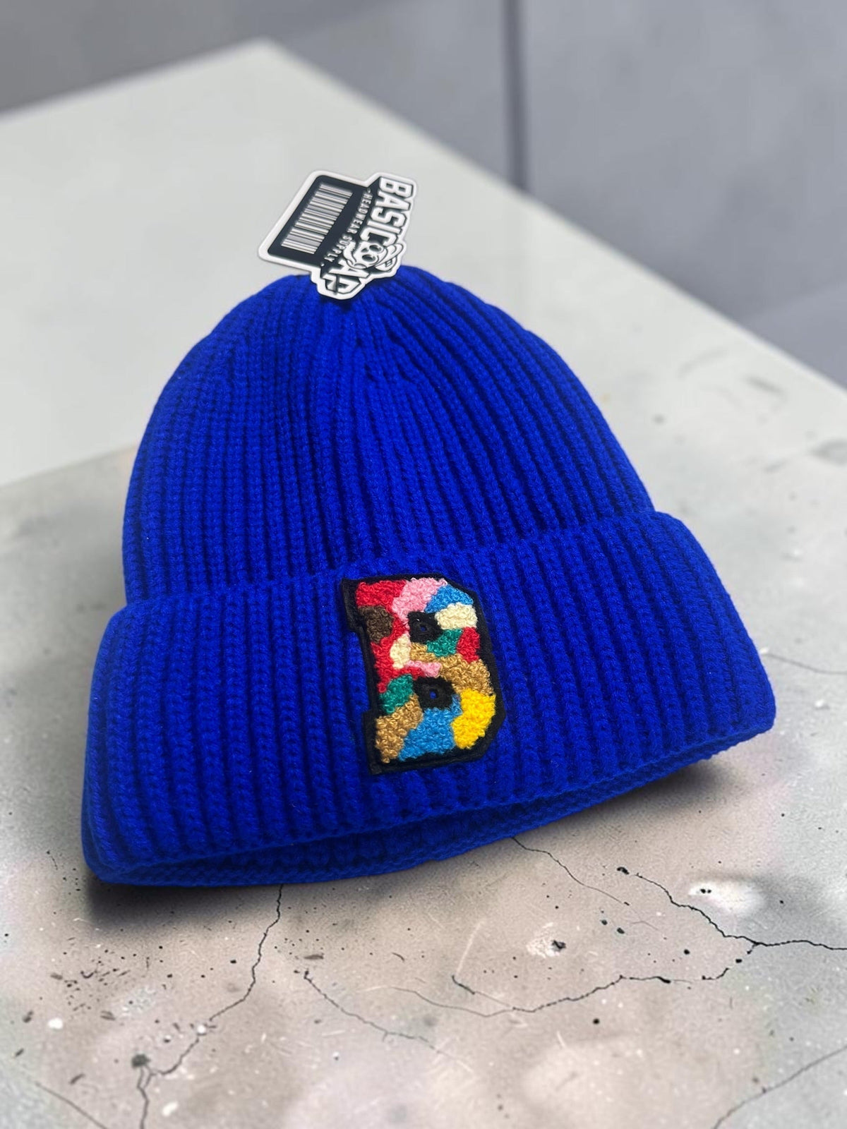 B-Is-TheBrand blue ribbed knit beanie with a vibrant multi-colored embroidered B patch on the front cuff.