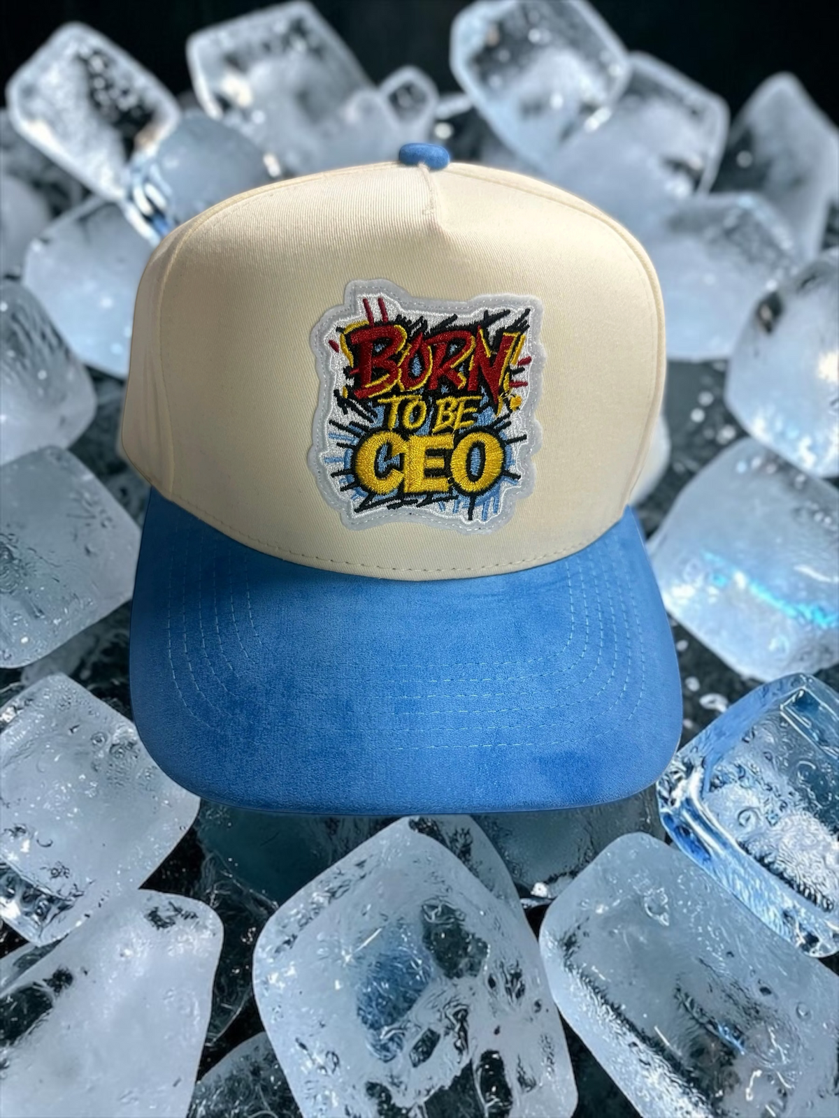 B-Is-TheBrand Born To Be CEO trucker hat with cream foam front, blue suede brim, and vibrant graffiti patch on ice.