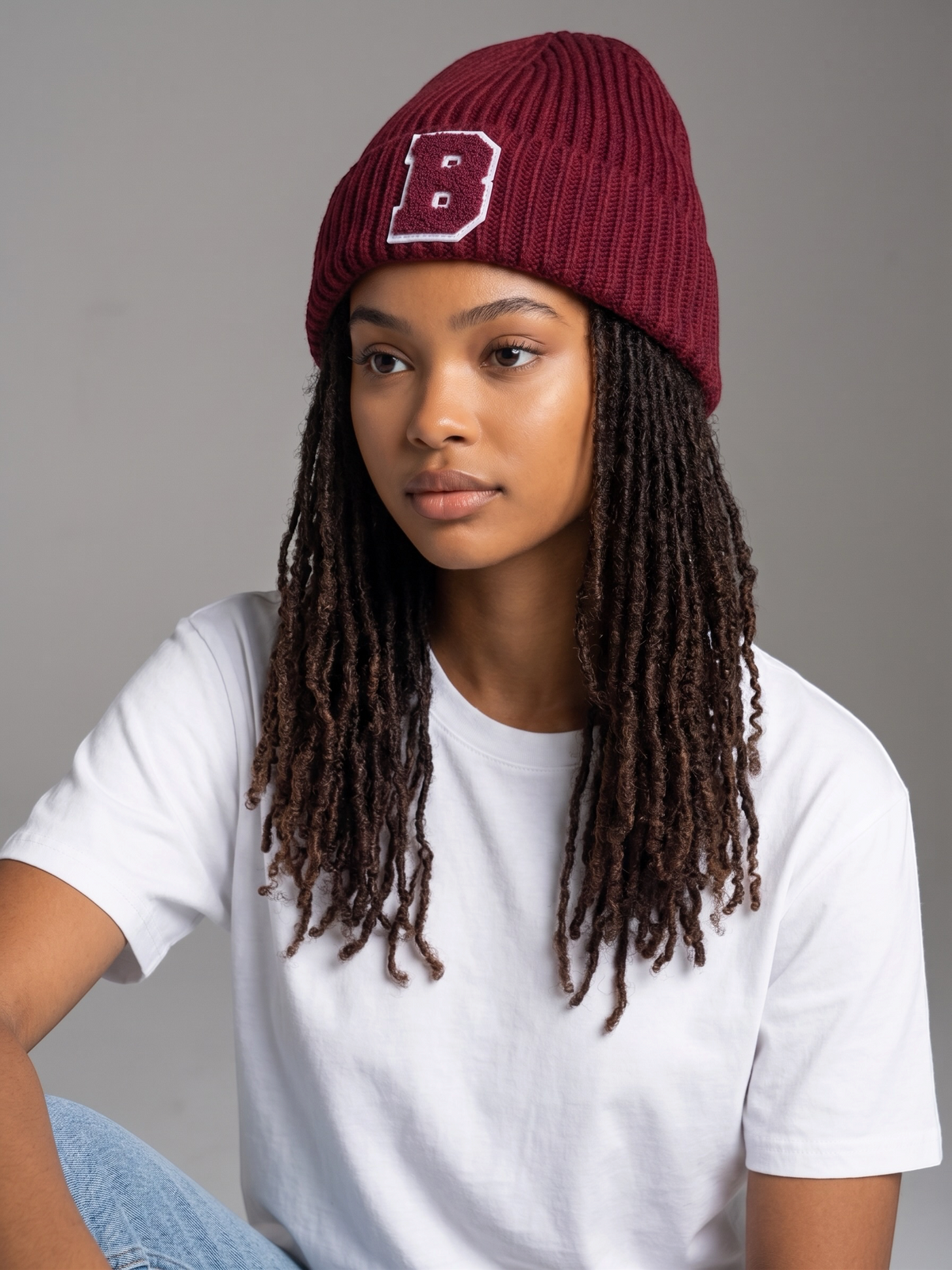 Model wearing a B-Is-TheBrand burgundy ribbed knit cuffed beanie with a varsity-style letter B patch.