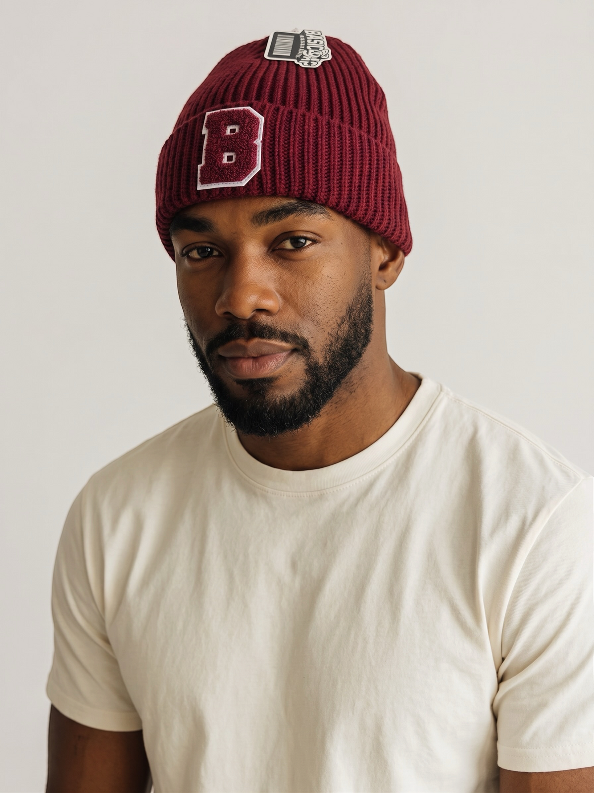 A man wearing a B-Is-TheBrand burgundy ribbed knit cuffed beanie with a varsity-style letter B patch.