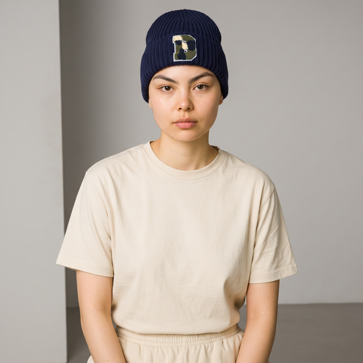A model wearing a B-Is-TheBrand navy blue ribbed knit winter beanie with a textured letter patch on the front.