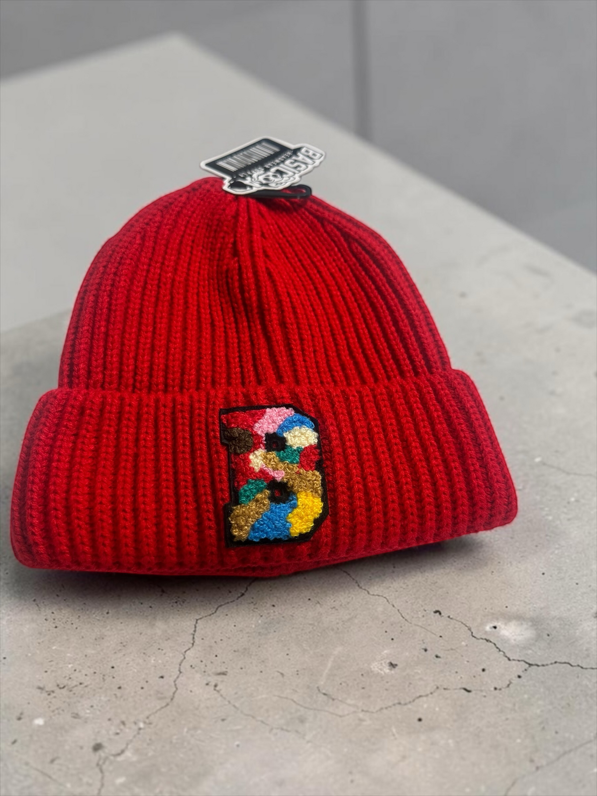 B-Is-TheBrand red ribbed knit beanie featuring a vibrant multi-colored embroidered B patch on the front cuff.