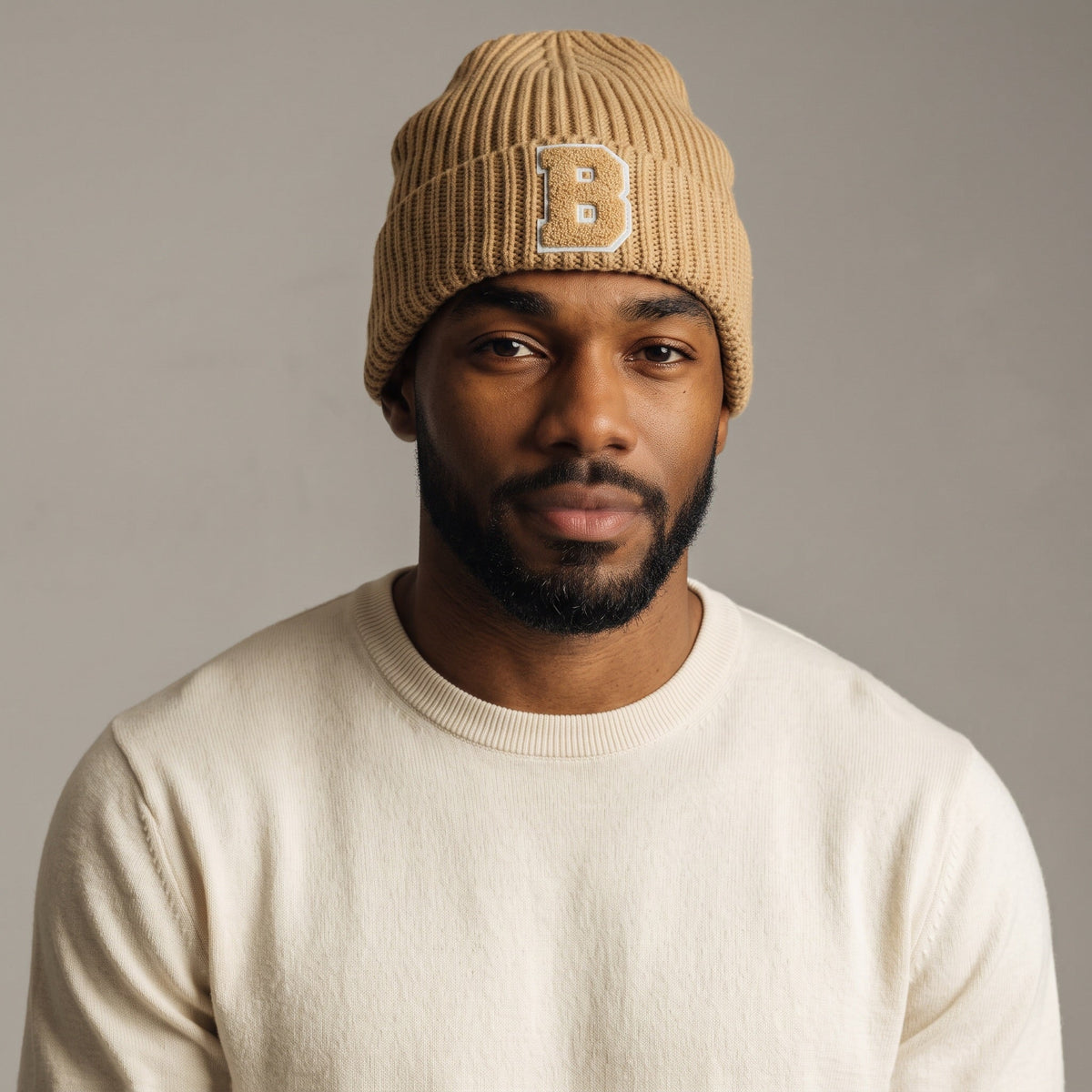 A man wearing a B-Is-TheBrand sand brown ribbed knit beanie with a textured B patch on a neutral background.